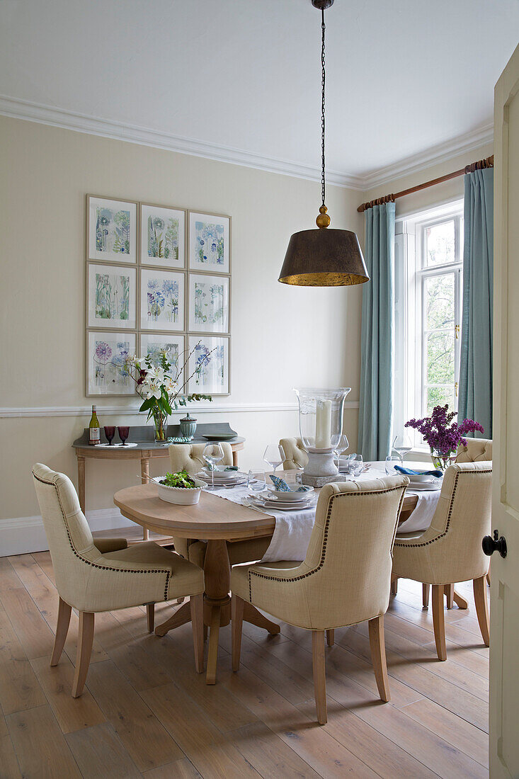 Cremefarbene gepolsterte Esszimmerstühle mit Messing-Pendelleuchte in einem Haus in Worcestershire, England, UK