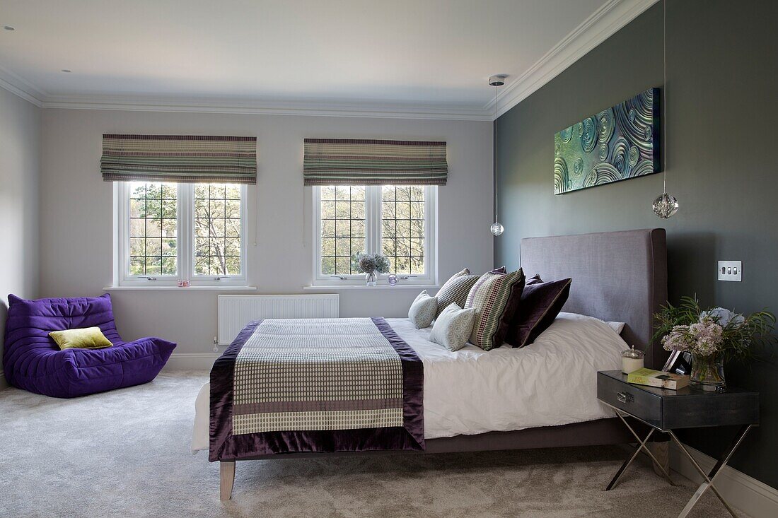 Double bed with quilted cover and purple armchair beside leaded windows in Sussex home England UK