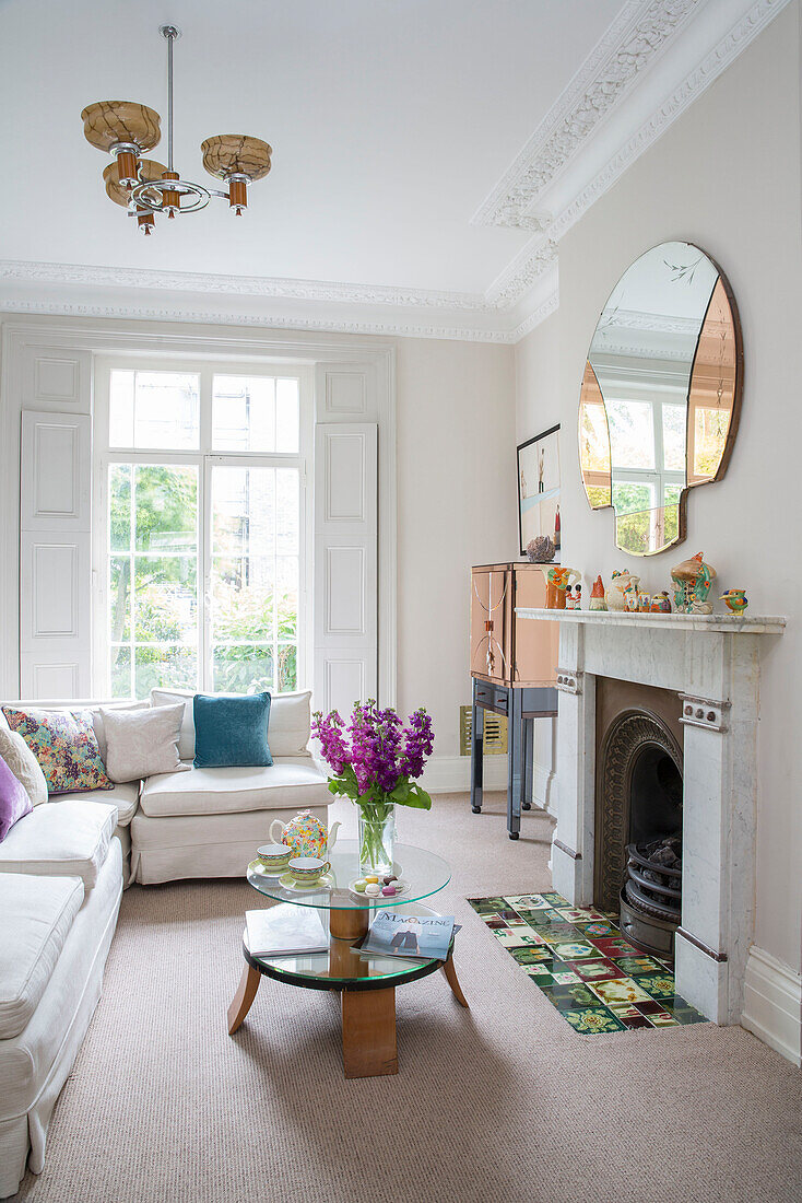 Schnittblumen auf Couchtisch mit Vintage-Spiegel über dem Kamin im Wohnzimmer eines Londoner Stadthauses UK