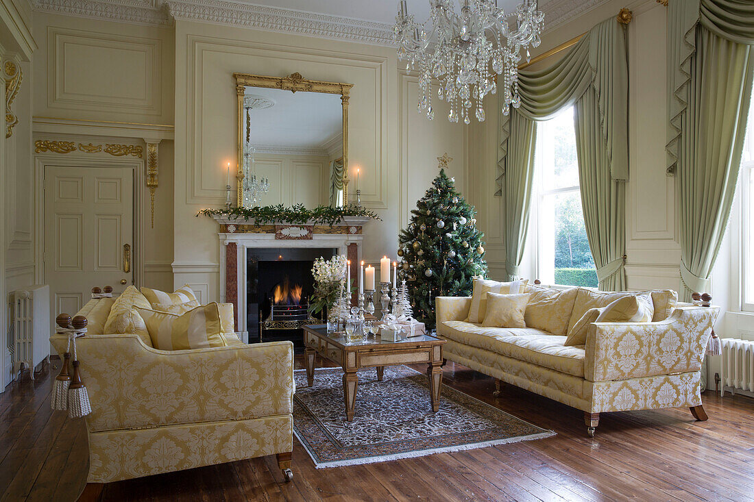 Cremefarbene und goldene Sofas mit beleuchtetem Kamin und Weihnachtsbaum in einem Landhaus in Kent, England UK