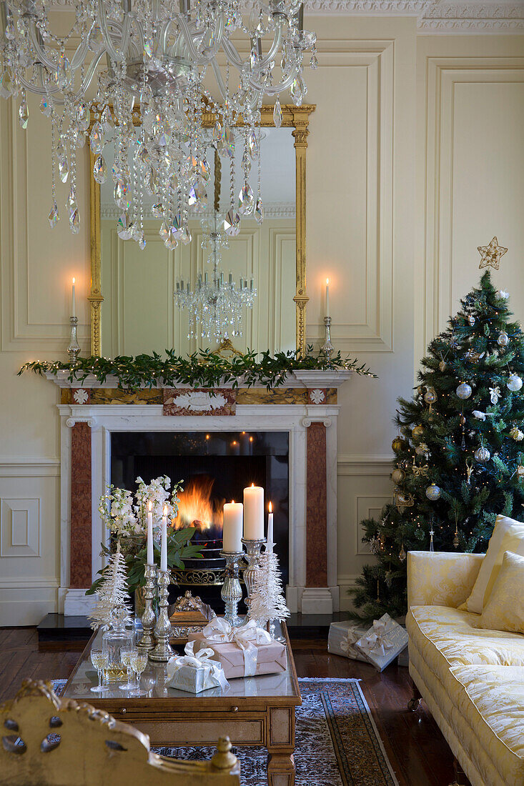 Kristalltropfen-Kronleuchter über dem Couchtisch mit beleuchtetem Feuer und Weihnachtsbaum in einem Landhaus in Kent England UK