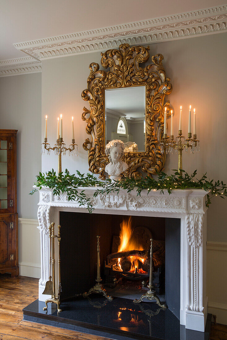 Lit fire with gilt-framed decorative mirror in Kent country house England UK
