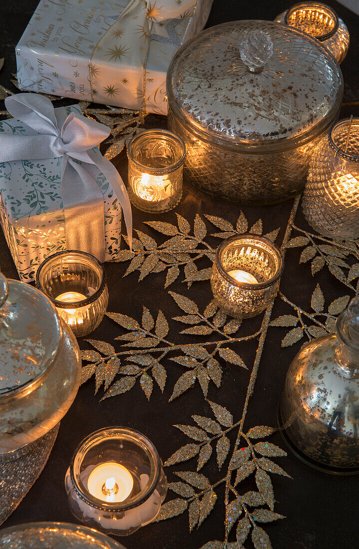 Beleuchtete Teelichter mit silbernen Blättern und mit Schleife verpackten Geschenken in Kent England UK