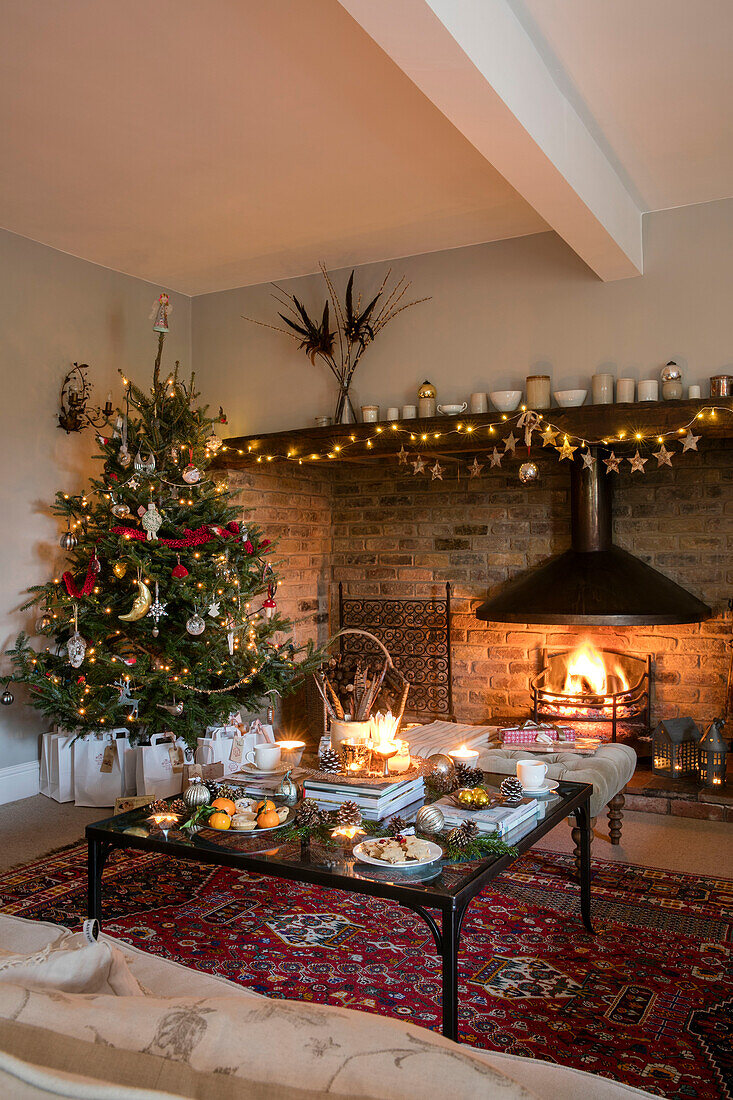 Gift bags below Christmas tree with fairylights on mantle above lit fire in Cheshire living room UK