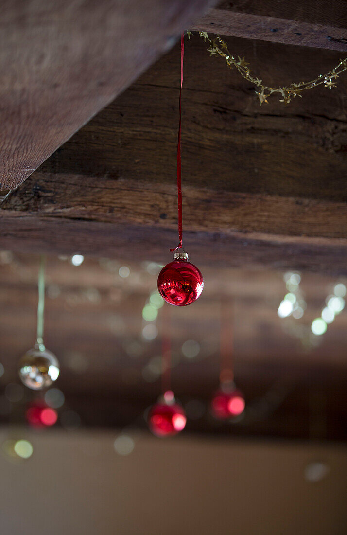 Red and silver baubles hang from timber-framed ceiling in Hampshire farmhouse England UK