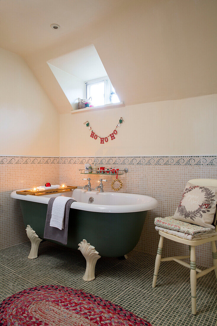 Freestanding bath below dormer window in mosaic tiled bathroom in Hampshire farmhouse England UK
