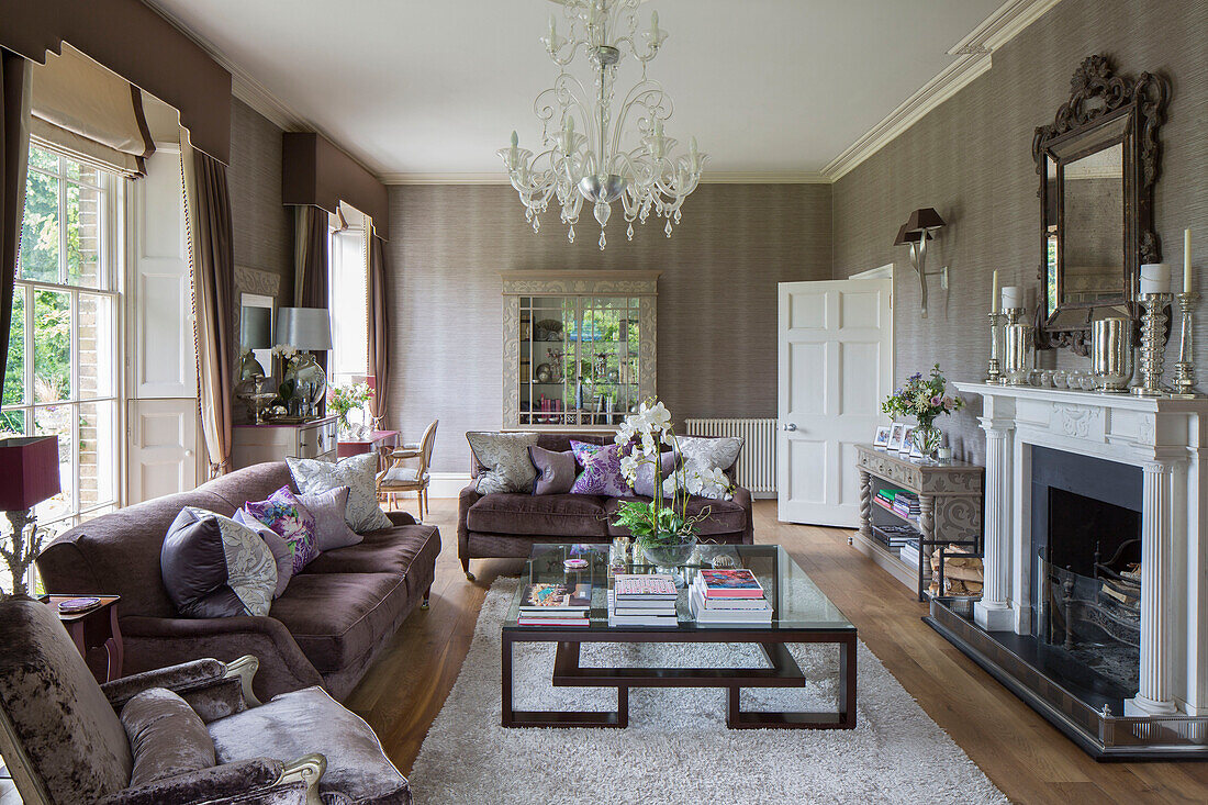 Braune Sofas mit gläsernem Couchtisch und Kronleuchter im Wohnzimmer eines Landhauses in Sussex, Großbritannien