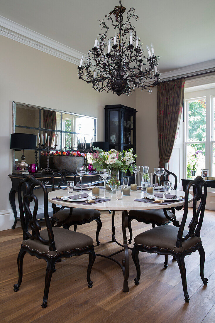 Dark dining chairs at circular table below chandelier in detached Sussex country house UK