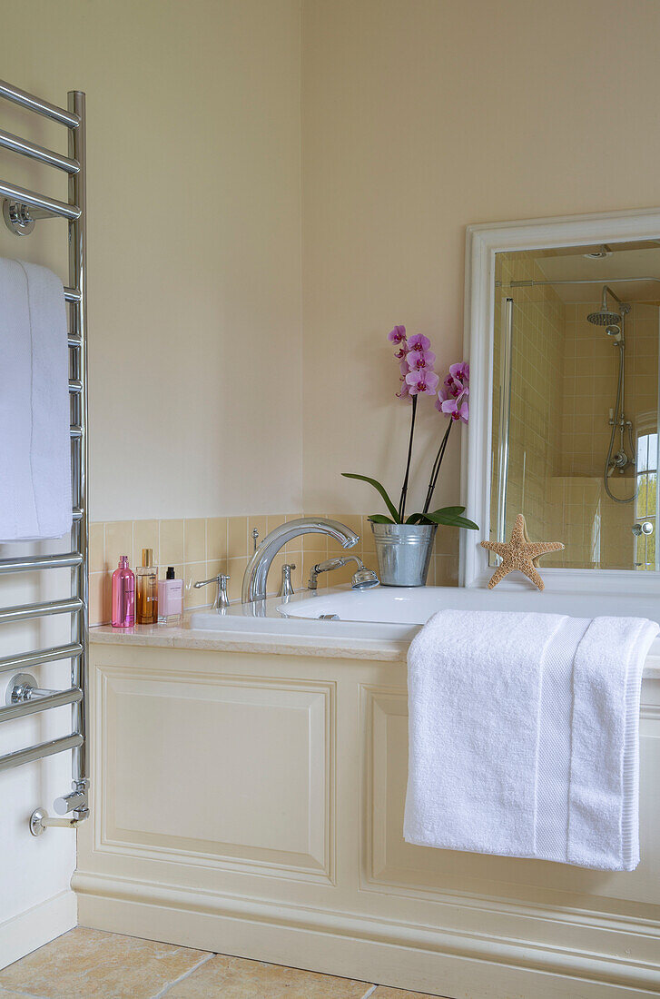Pinkfarbene Orchidee und Spiegel auf Badewanne mit wandmontiertem Heizkörper in einem umgebauten Bauernhaus in Kent, England