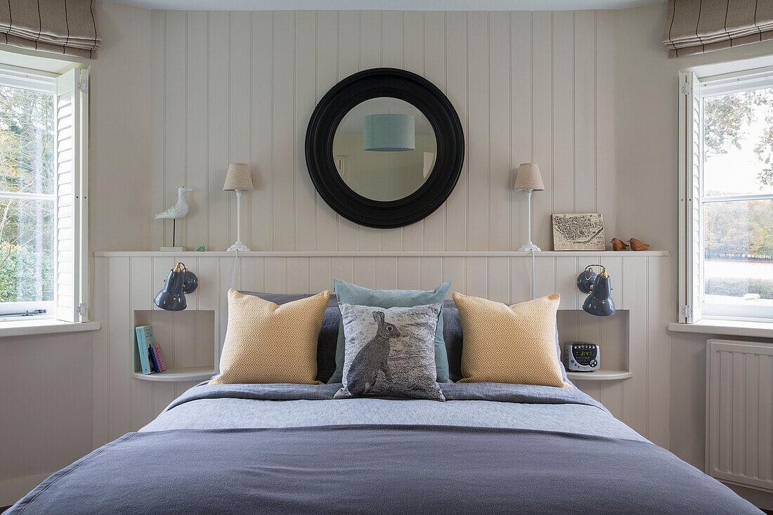 Black circular mirror on panelled wall above double bed in Oast house conversion Kent UK