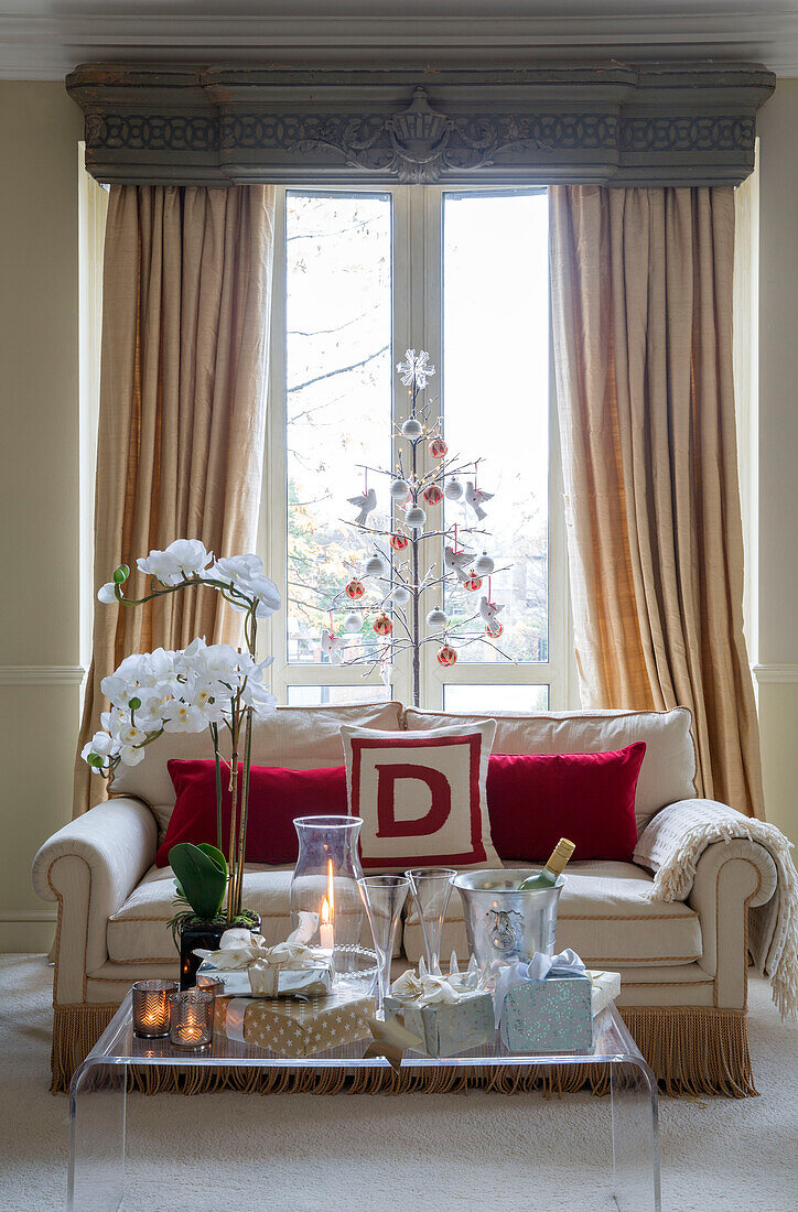 Two seater sofa with Christmas tree and orchid in window of London townhouse UK
