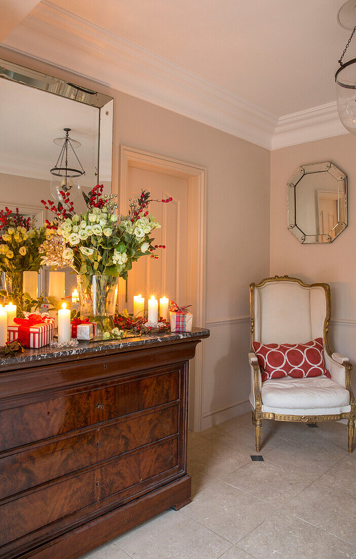 Schnittblumen und brennende Kerzen auf antiker Kommode mit vergoldetem Sessel in einem Londoner Stadthaus UK