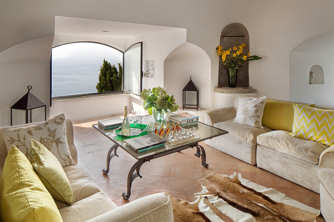Gelbe Kissen auf cremefarbenen Sofas mit gläsernem Couchtisch und Blick auf das Meer in einer Villa an der Küste von Amalfi, Italien