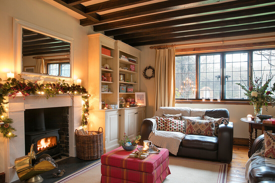 Two seater sofa with ottoman at lit woodburning stove with fairylit garland in Berkshire home UK