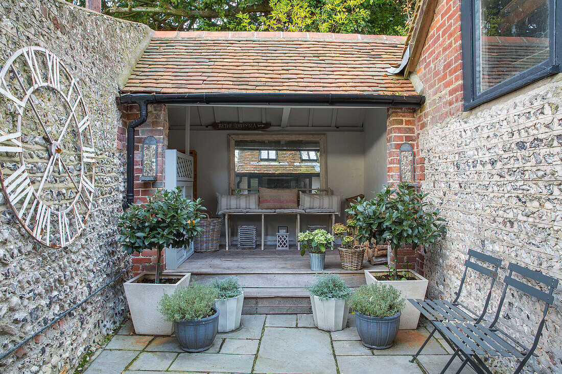 Große Uhr und Kübelpflanzen im Innenhof eines Sommerhauses in West Sussex