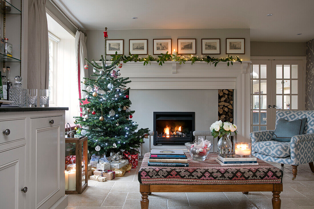 Weihnachtsbaum mit Geschenken und beleuchtetem Feuer im Wohnzimmer eines Bauernhauses in Dorset UK