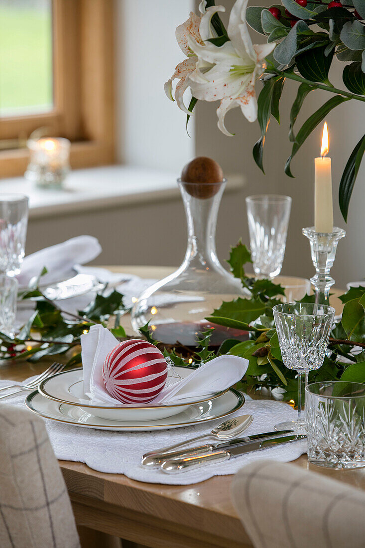 Christmas bauble on place setting with glassware and holly in Dorset farmhouse UK