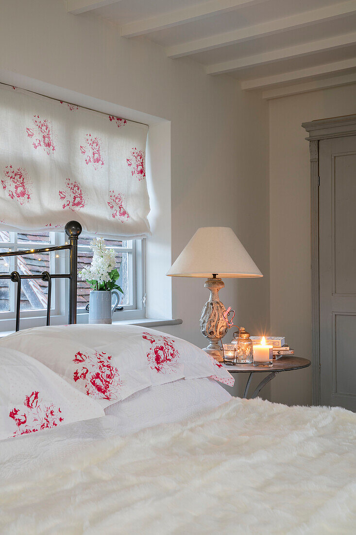 Geblümte Kissen mit passender Jalousie am Fenster mit Doppelbett und Lampe in einem Bauernhaus in West Sussex, Großbritannien