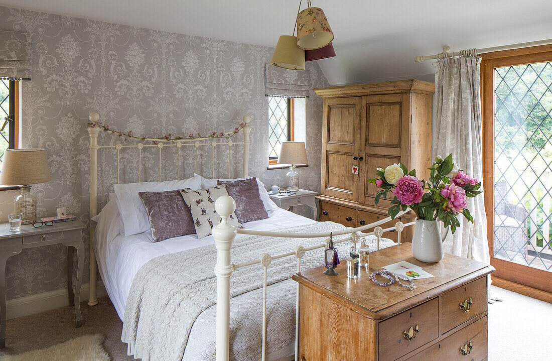 Cut flowers on wooden chest of drawers and matching lamps at bedside in detached 1950s house Alford Surrey UK