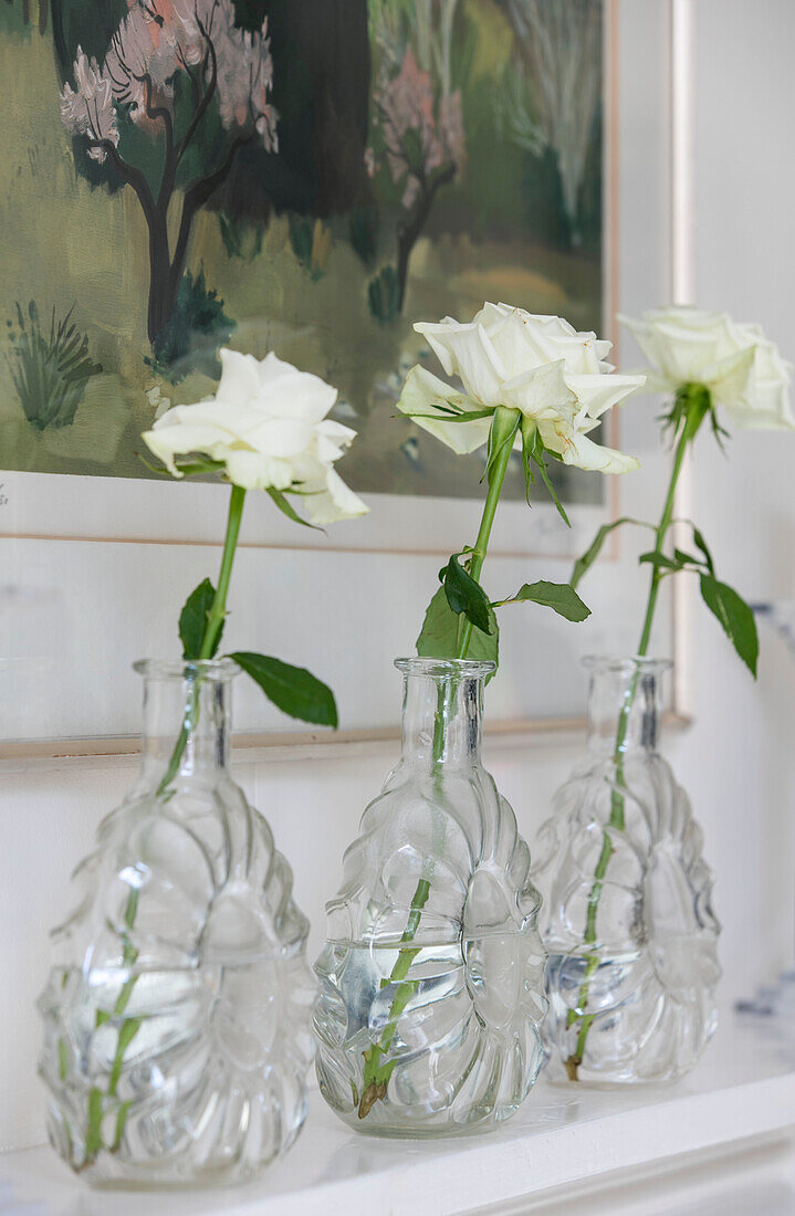 Weiße einstielige Rosen in Glasvasen auf einem Regal mit Kunstwerken in einem Stadthaus in West Sussex UK