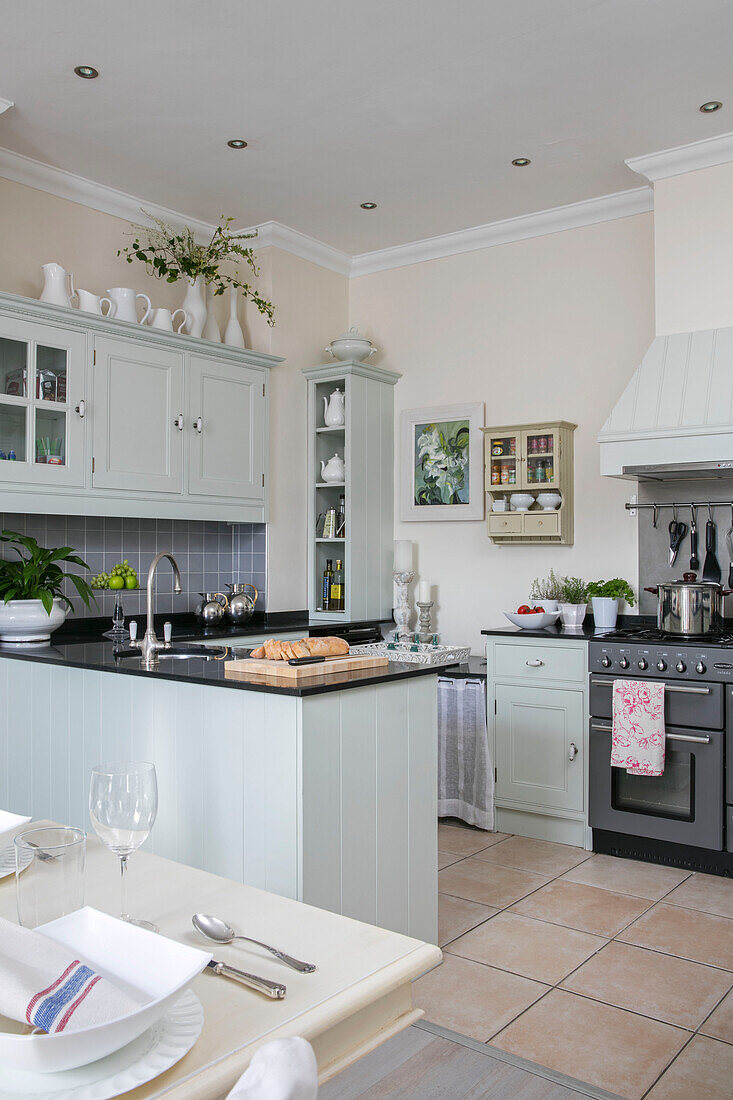 Light green fitted open plan kitchen with place setting at table in West Sussex townhouse UK