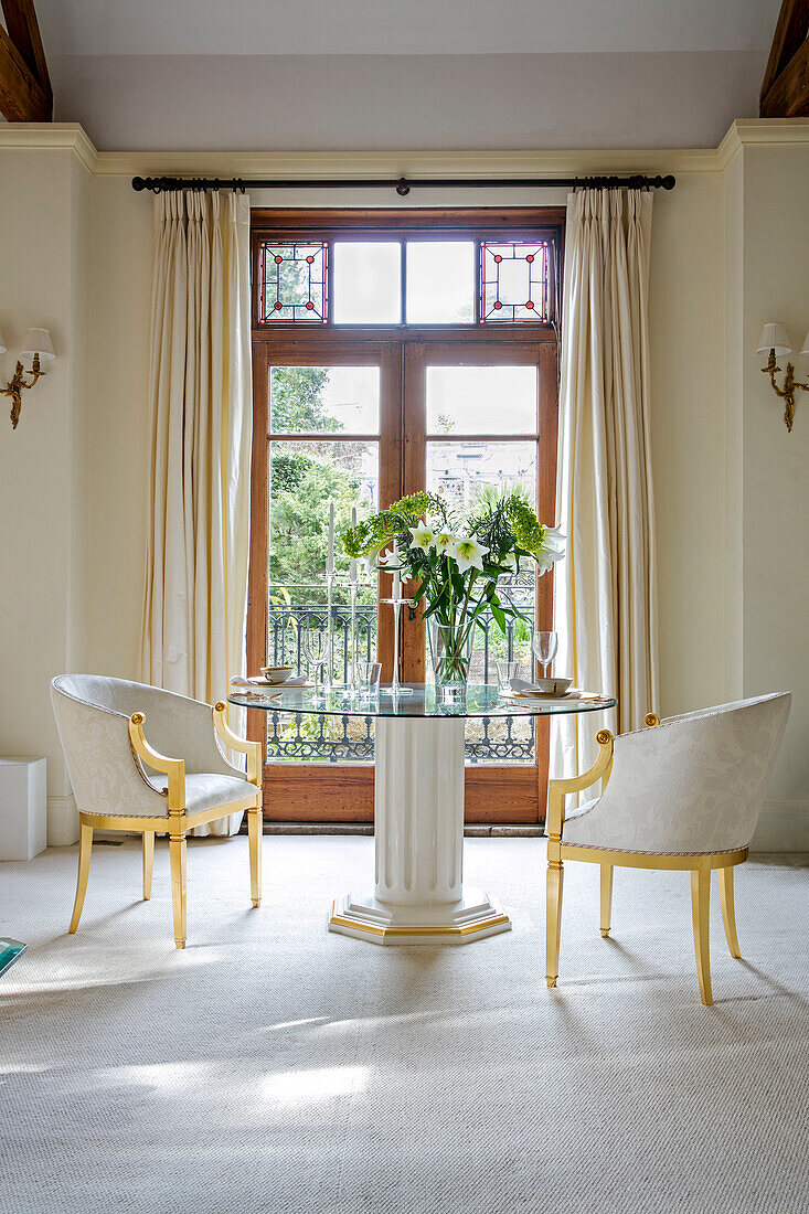 Pair of gilt chairs at glass topped table in double doorway of West Sussex townhouse UK