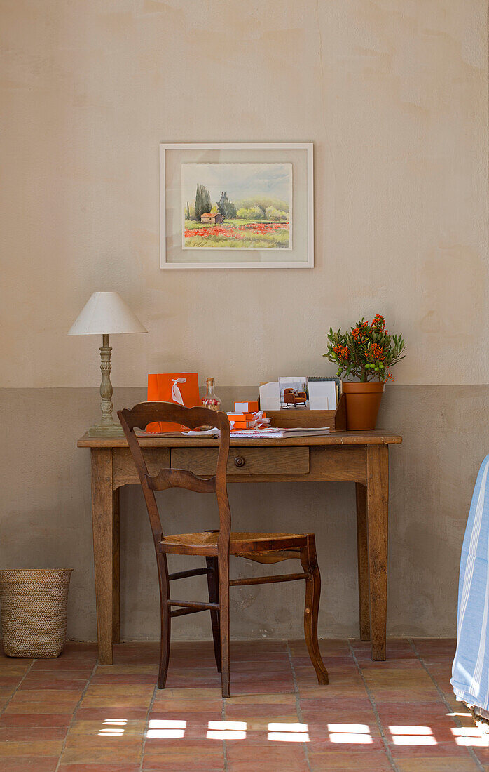 Letter rack and lamp on desk below artwork with sunlit terracotta floor in 19th century Provencal farmhouse France