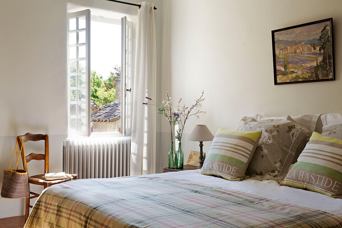 Gestreifte Kissen auf kariertem Bett am offenen Fenster mit Stuhl in einem provenzalischen Bauernhaus aus dem 19