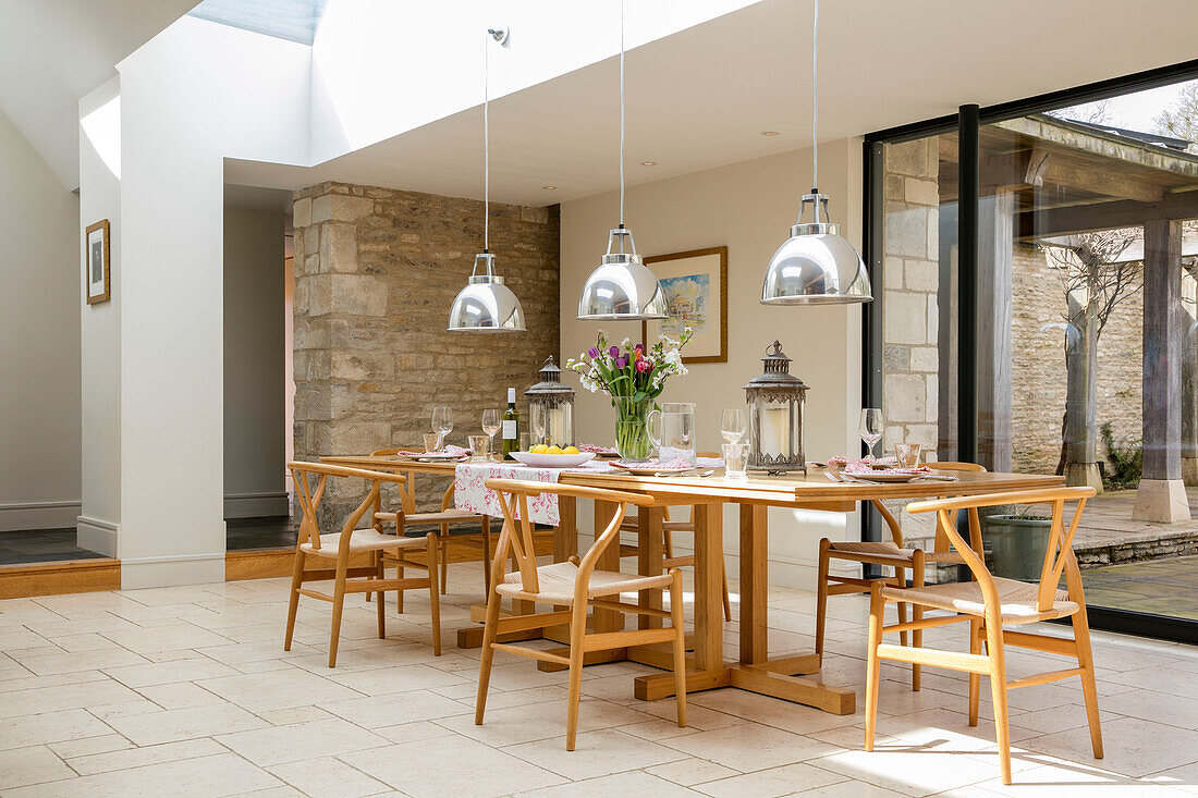 Chrome pendant shades hang above wooden dining table and chairs in Gloucestershire barn conversion UK