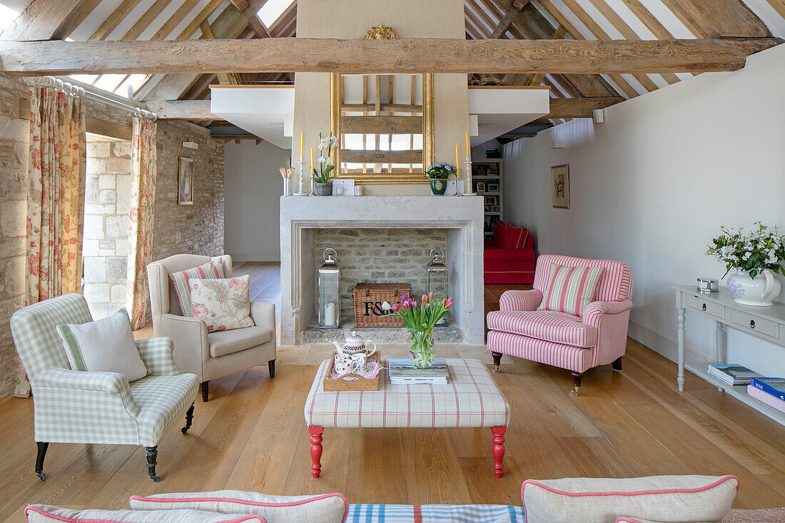 Armchairs and ottoman with gilt framed mirror in beamed living room in Gloucestershire barn conversion UK