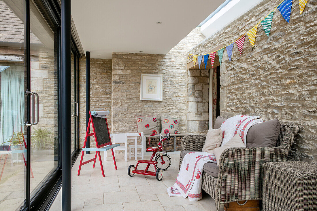 Kreidetafel und Dreirad mit Zweisitzer-Sofa und Wimpel in einer umgebauten Scheune in Gloucestershire UK