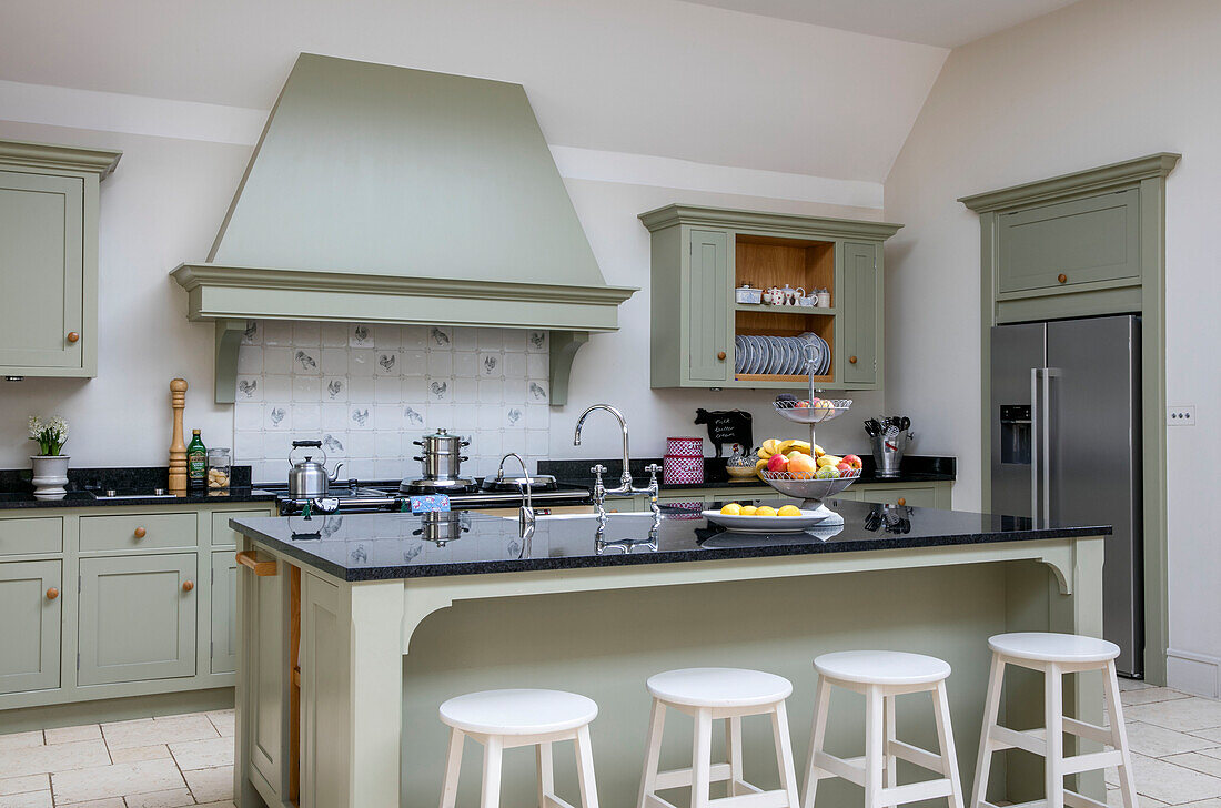 White stools at breakfast bar in kitchen with light green extractor Gloucestershire barn conversion UK