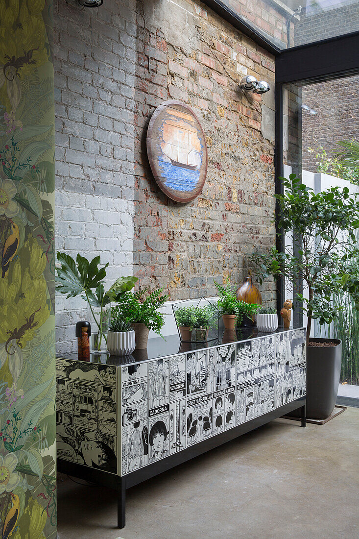 Zimmerpflanzen auf einem Pop-Art-Sideboard mit freiliegender, teilweise bemalter Ziegelwand in einem viktorianischen Stadthaus in London UK