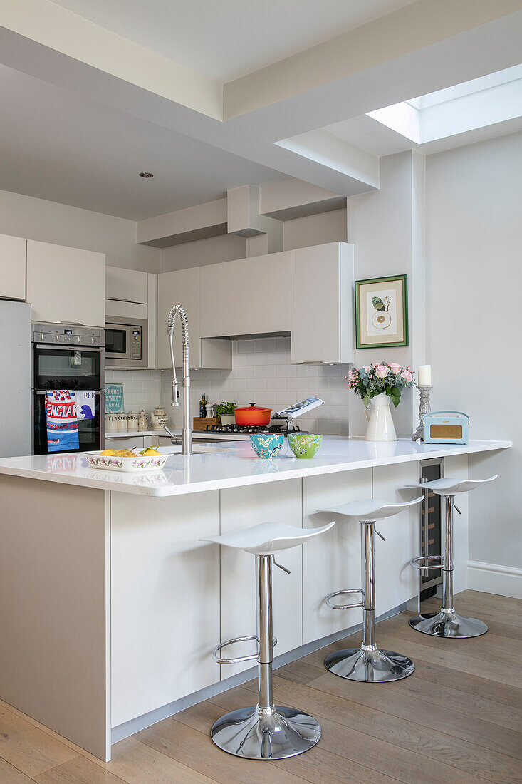 Stools at breakfast bar in modern white kitchen of London home UK