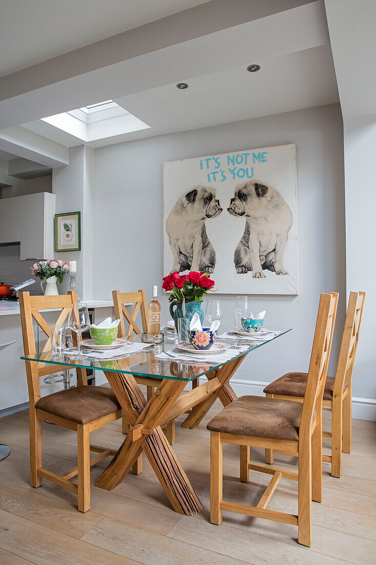 Holzstühle an einem Esstisch mit Glasplatte und einem großen Kunstwerk mit Bulldoggen in einem Haus in London UK