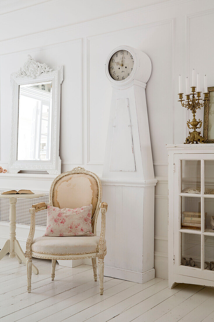 Cream armchair and Gustavian clock with mirror and cabinet in Edwardian house Surrey UK