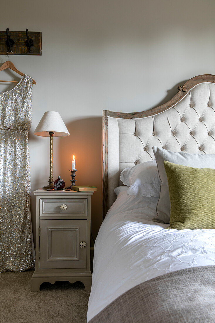 Sequinned dress hanging at bedside with lit candle in Hampshire home