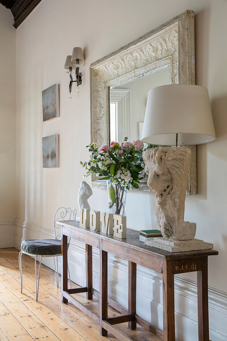 "Weiße Lampe und großer Spiegel über einer Holzkonsole mit Schnittblumen und dem Wort LOVE"" in einem freistehenden Haus in Kent, Großbritannien"""