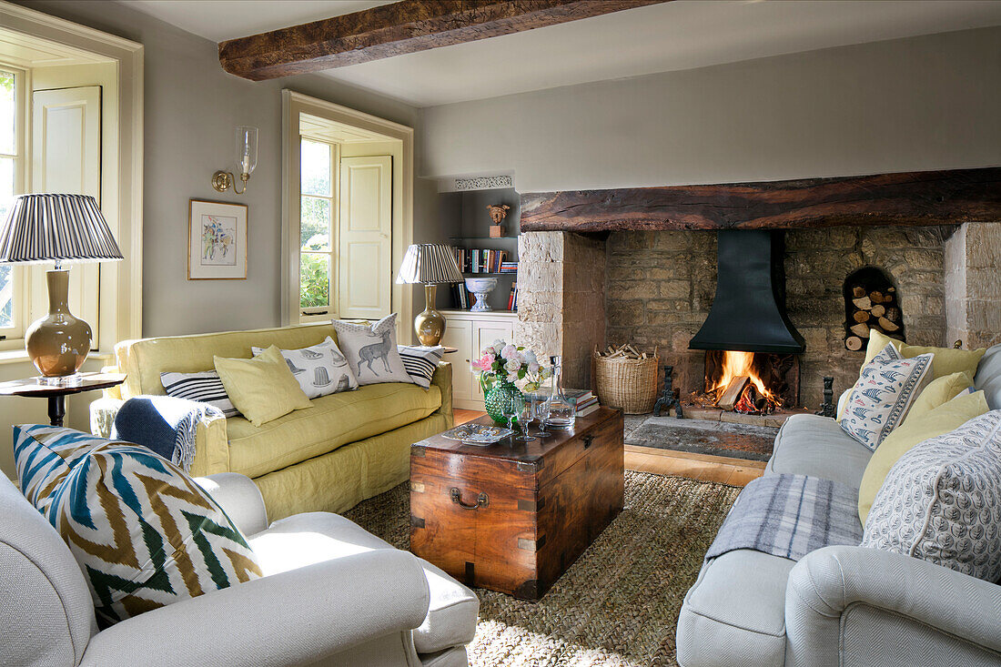 Gelbes Sofa und Lampen mit Holztruhe vor beleuchtetem Kamin in einem Haus in Somerset, UK