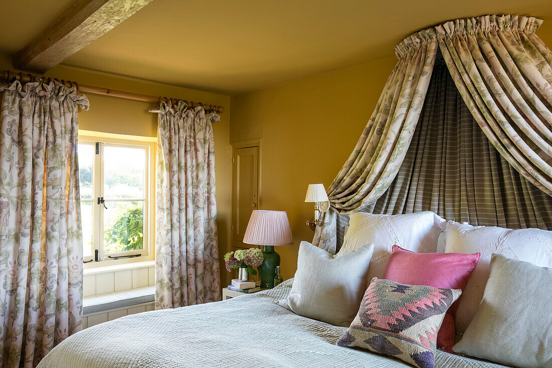 Double bed with co-ordinated canopy at window in yellow room Somerset bedroom UK