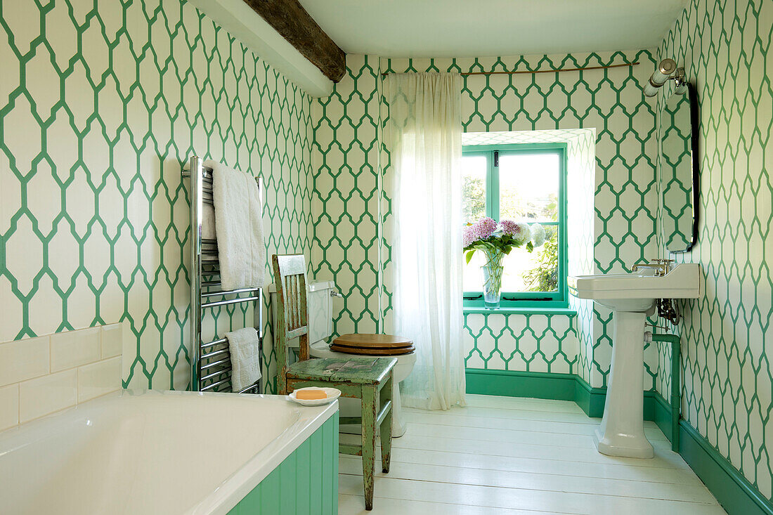 Green and white patterned wallpaper with chrome towel rail and bath in Somerset home UK