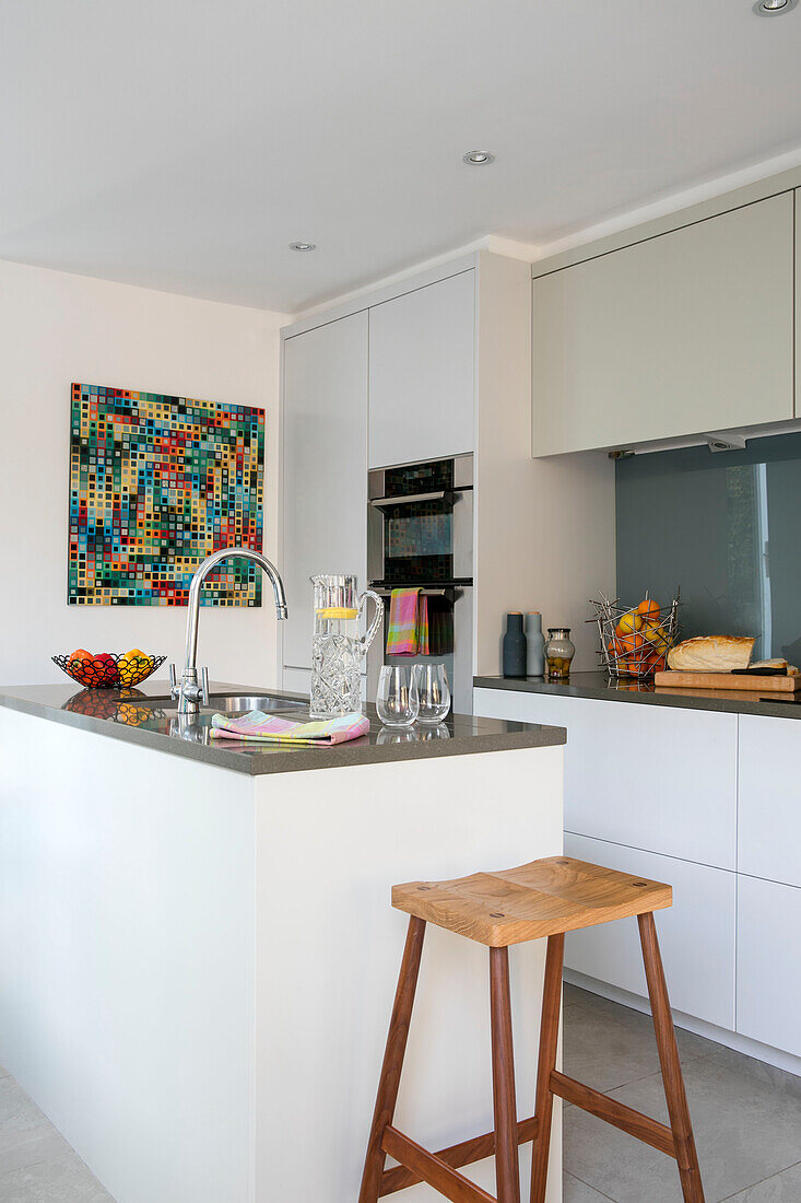 Holzhocker an der Kücheninsel mit moderner Kunst in einem Haus in London UK