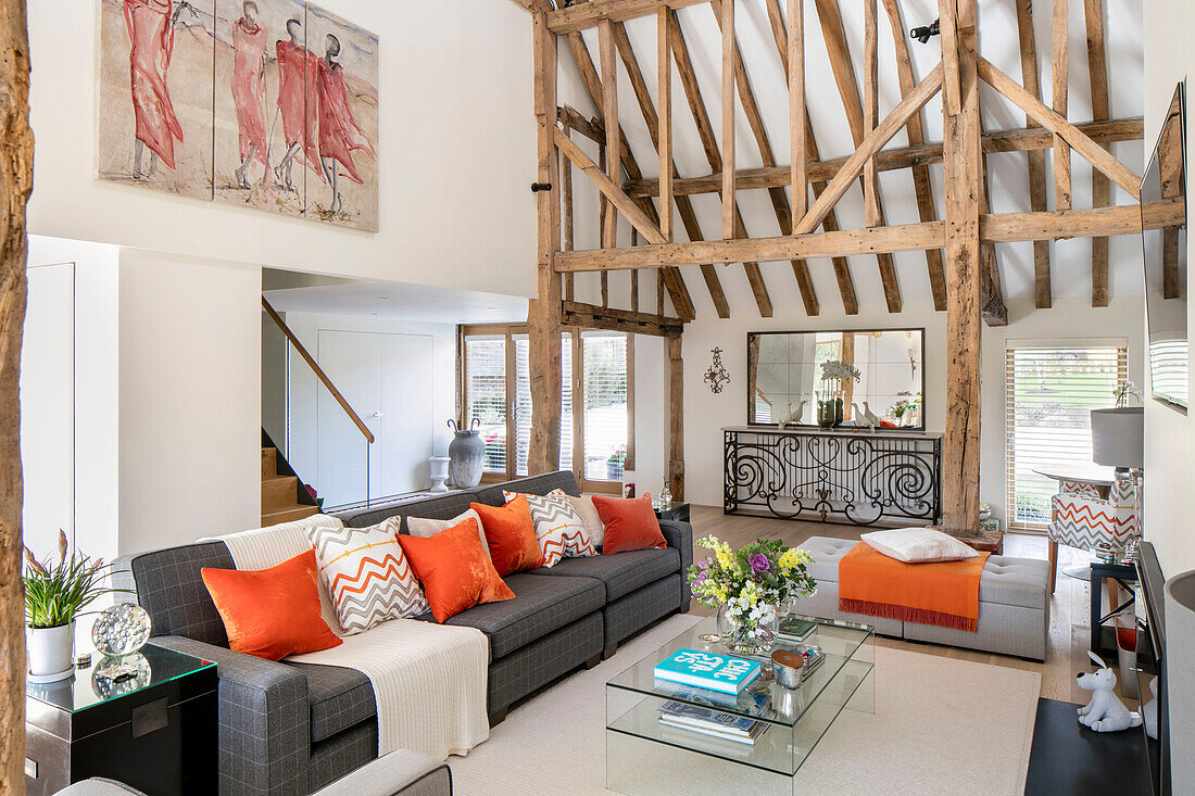 orange cushions on sofa with glass table and beamed ceiling in Hampshire home UK
