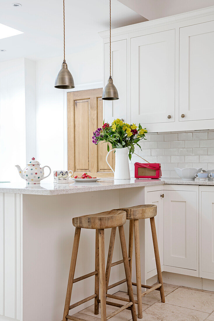Messing-Pendelleuchten über der Frühstücksbar mit Holzhockern in einer Küche in Hampshire UK