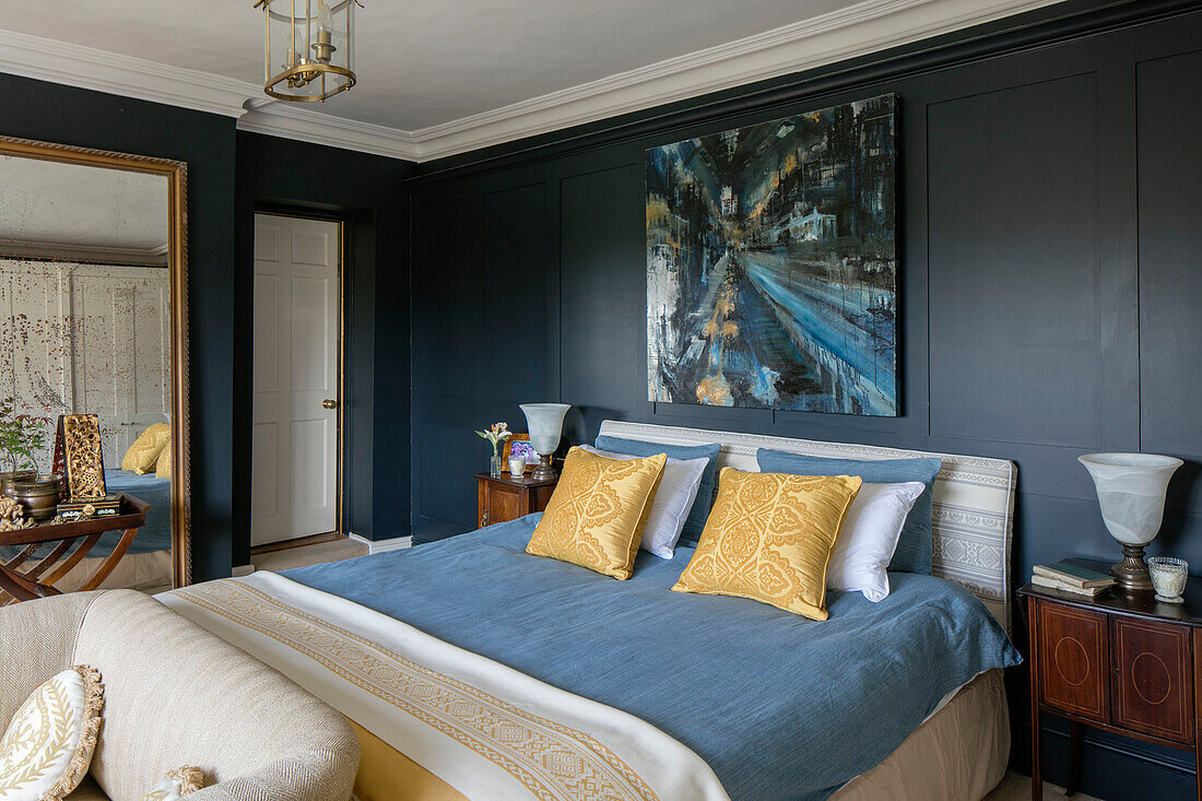 Kunstleinwand und großer Spiegel im blau getäfelten Schlafzimmer eines Cottage in Kent UK