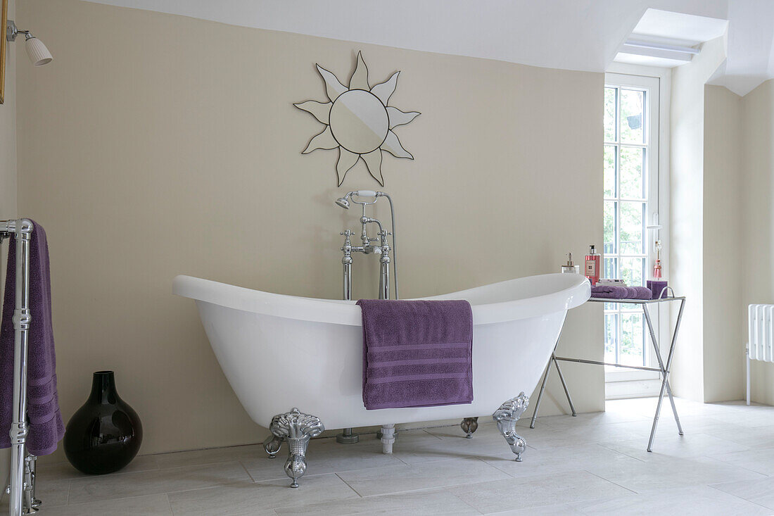 Lila Handtücher mit freistehender Badewanne und Spiegel mit Sonnenschliff im Badezimmer in Sussex, Großbritannien