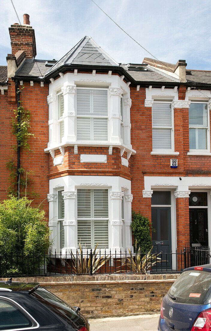 Cars parked outside London terraced house with white paintwork on bay windows UK