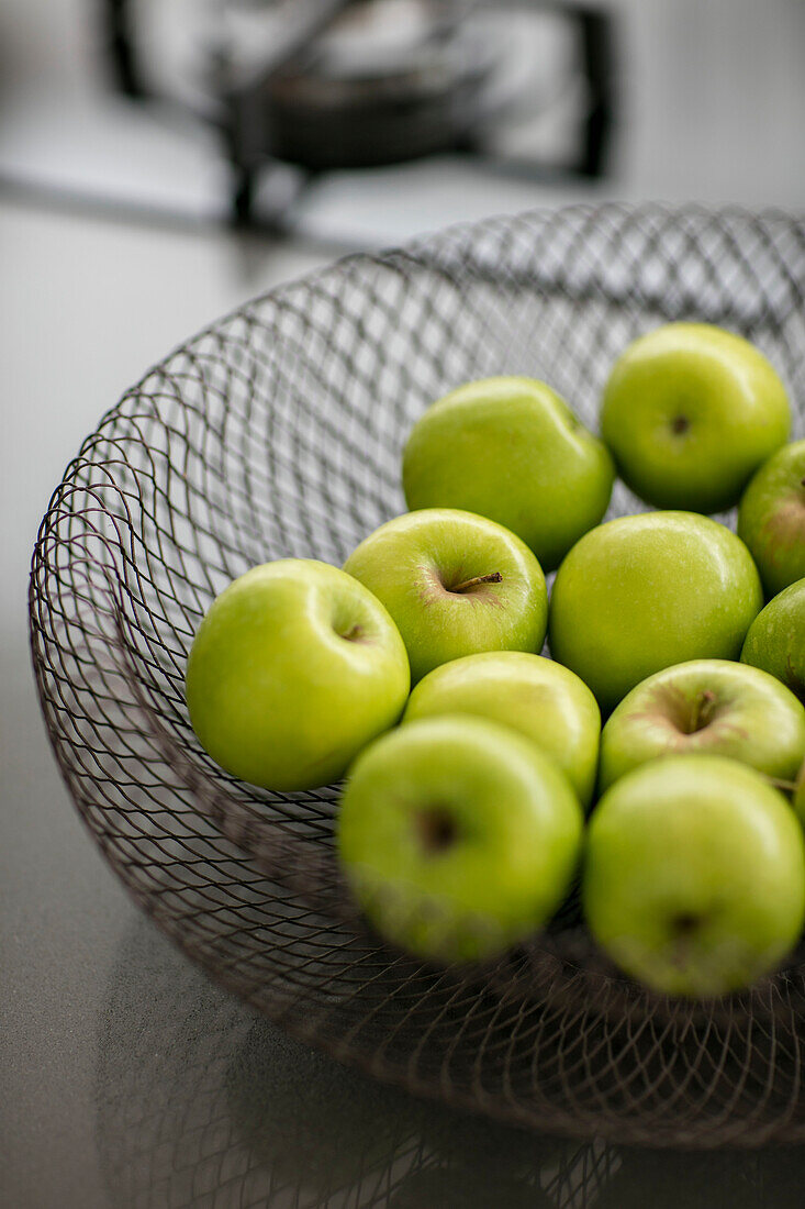 Korb aus Drahtgeflecht mit leuchtend grünen Äpfeln in einem Londoner Haus UK