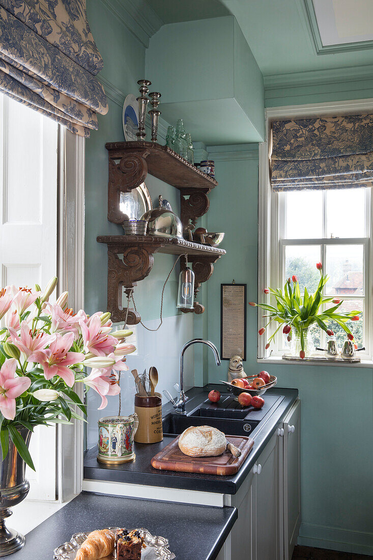 Lilien und Tulpen in der Küche mit geschnitzten Holzregalen und Raffrollos in einem Haus in Sussex
