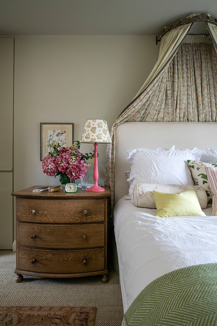 Rosa Lampe und Blumen auf hölzerner Kommode am Bett in einem Londoner Haus UK